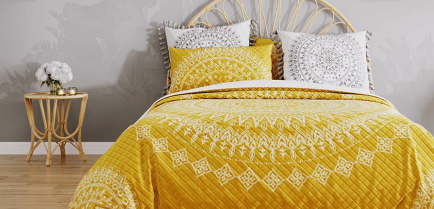 Lit en bois vintage avec linge de lit jaune, table basse en bois, fleurs et bougies 